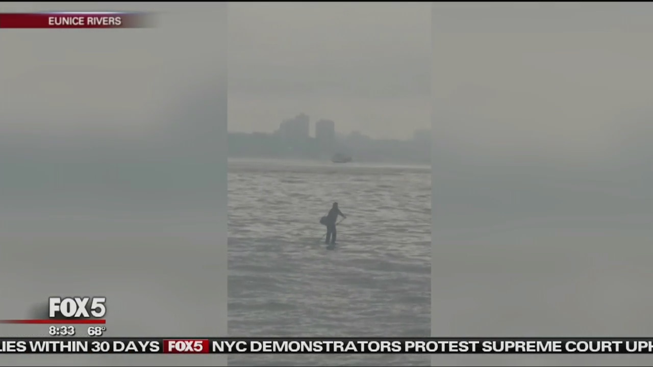 Man Paddleboards in Suit Across River